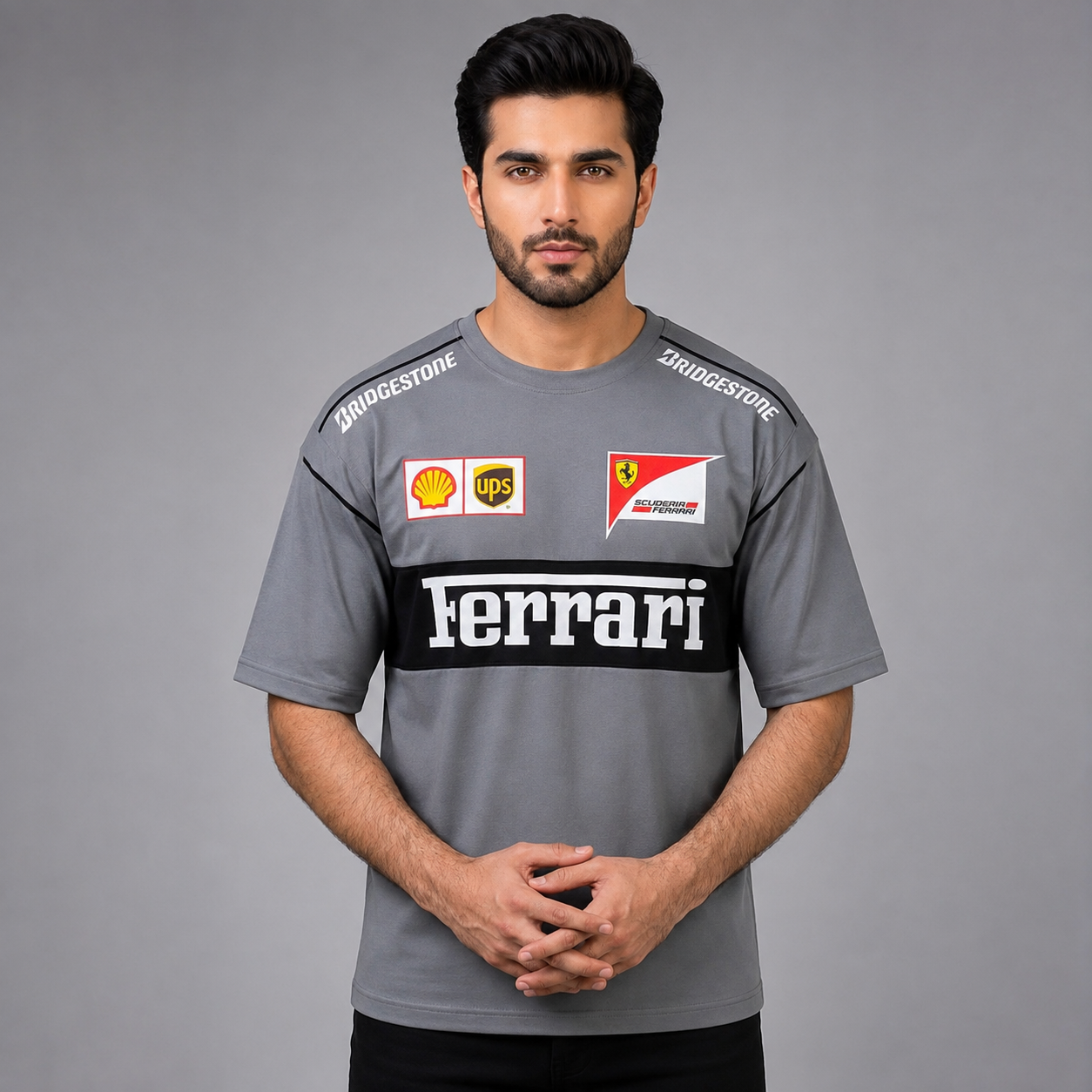 A man wearing a gray Ferrari team t-shirt with sponsor logos including Bridgestone, UPS, and Shell, set against a solid gray studio background.