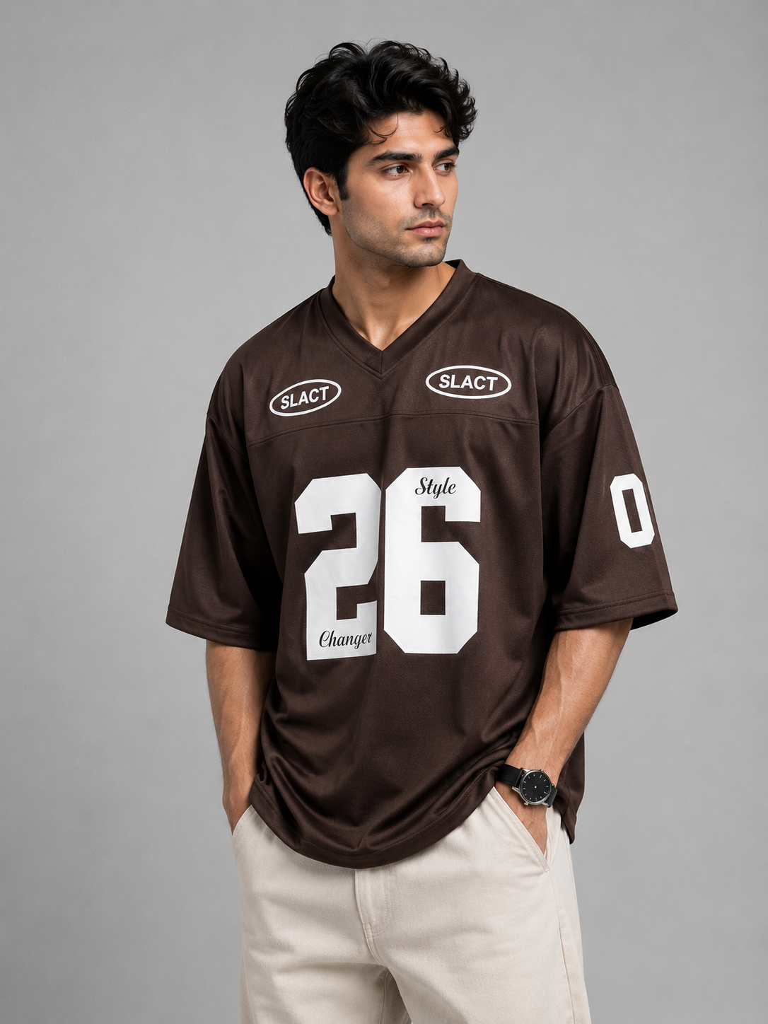 A man wearing a dark brown football-style jersey with large white '26' on the front, 'SLACT' logos on the chest, and 'Style Change' text, paired with light beige pants against a gray studio background.