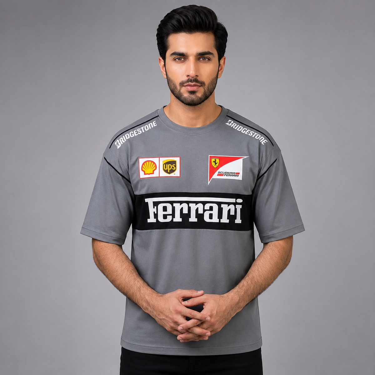 A man wearing a gray Ferrari team t-shirt with sponsor logos including Bridgestone, UPS, and Shell, set against a solid gray studio background.