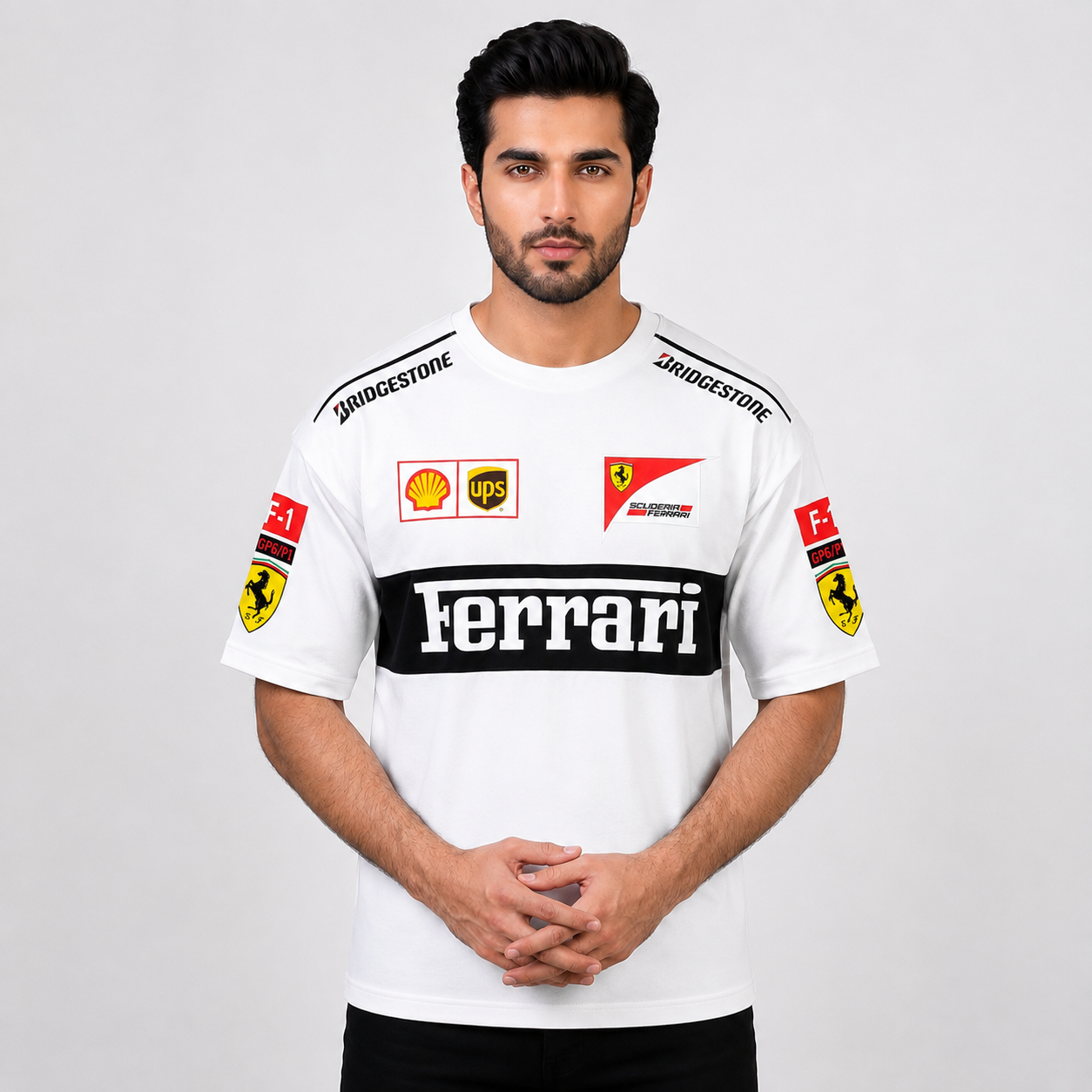 A man wearing a white Ferrari team t-shirt with sponsor logos including Bridgestone, UPS, Shell, and Ferrari, photographed against a light gray studio background.