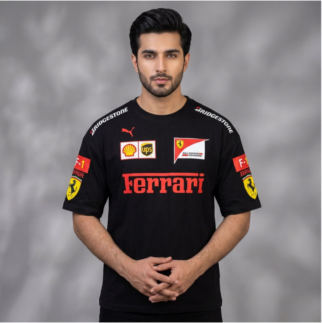 A man wearing a black Ferrari short-sleeve sports jersey with red and yellow sponsor logos, including Bridgestone, Puma, Shell, and UPS, standing against a gray studio background.