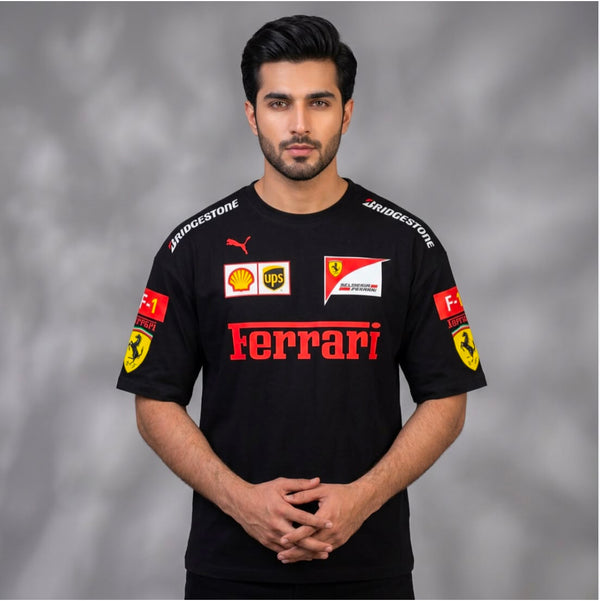 A man wearing a black Ferrari short-sleeve sports jersey with red and yellow sponsor logos, including Bridgestone, Puma, Shell, and UPS, standing against a gray studio background.